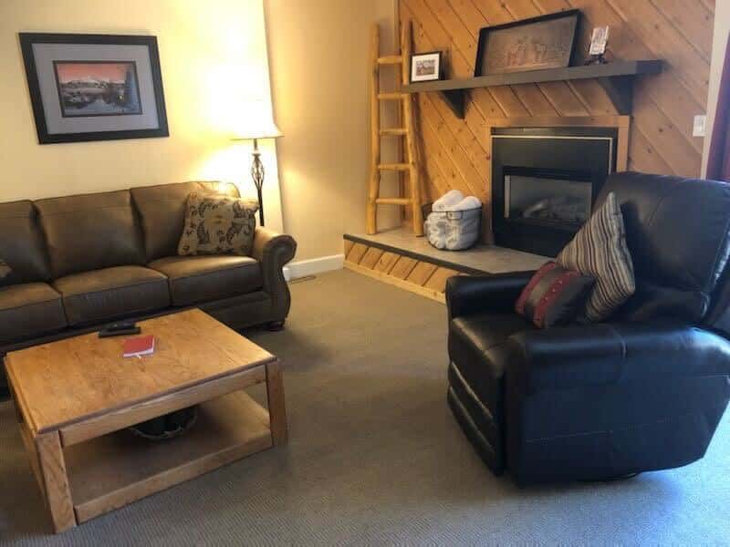 The cozy living area is full of classic cabin charm and ample plush seating between two couches, a coffee and a comfortable recliner, all surrounding the striking wood-paneled fireplace.