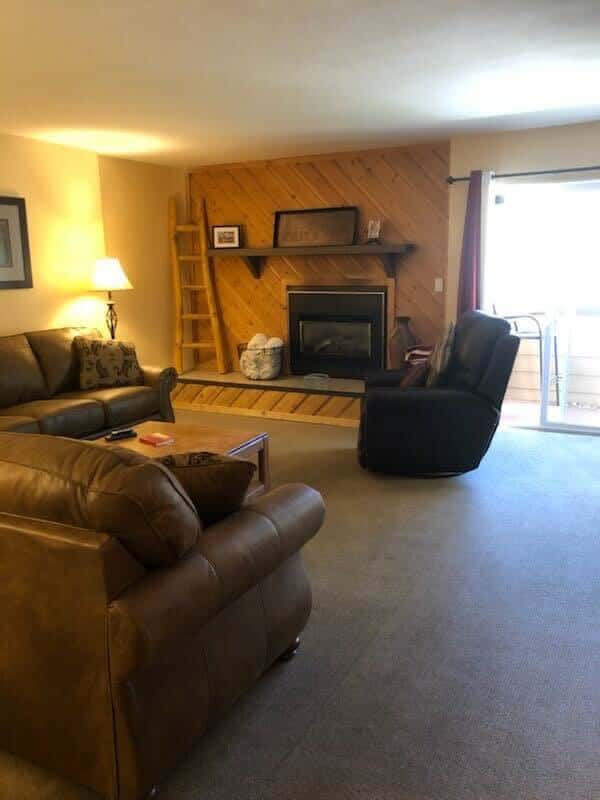 The cozy living area is full of classic cabin charm and ample plush seating between two couches, a coffee and a comfortable recliner, all surrounding the striking wood-paneled fireplace.