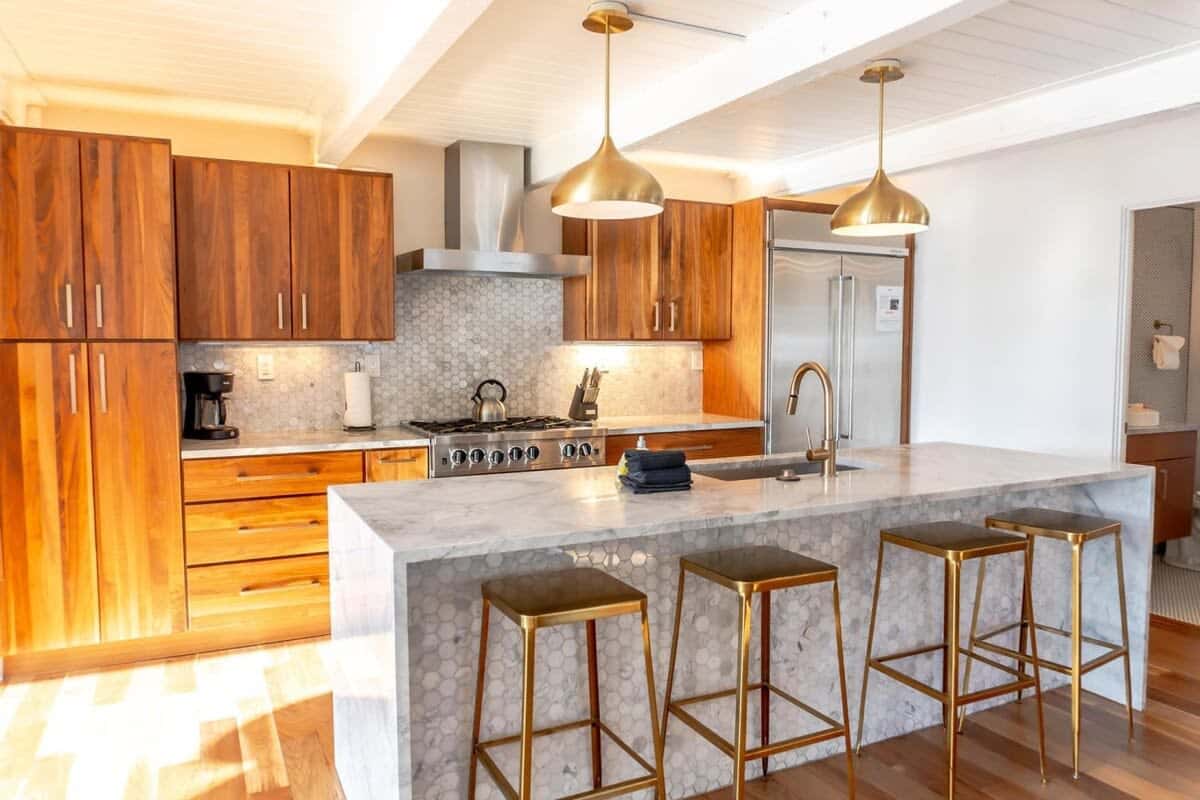The modern fully equipped kitchen is an open and beautiful space with high-end stainless steel appliances, ample counter space, and a large kitchen island with four bar stools.