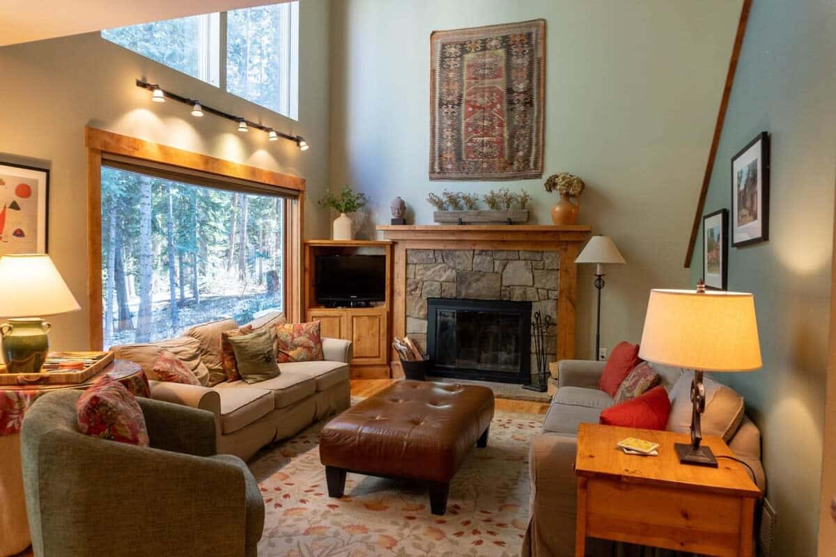 This charming home's bright and open living room features high ceilings and spacious windows perfect for watching the snowfall or enjoying the nature views as you relax by the fire.