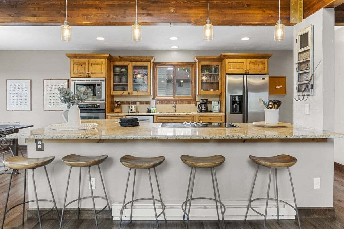 The kitchen is a charming and efficient space with classic wood cabinets, exposed wood beams, stainless steel appliances, and a large kitchen bar opening out to the living room.
