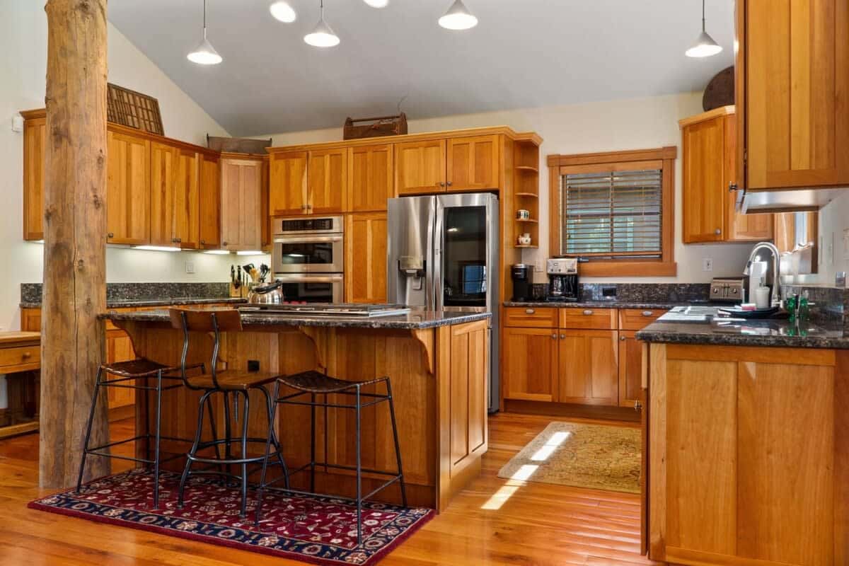 The fully equipped kitchen features high-end appliances, a large kitchen island with three barstools, ample cabinet and counter space, and classic wood finishes.