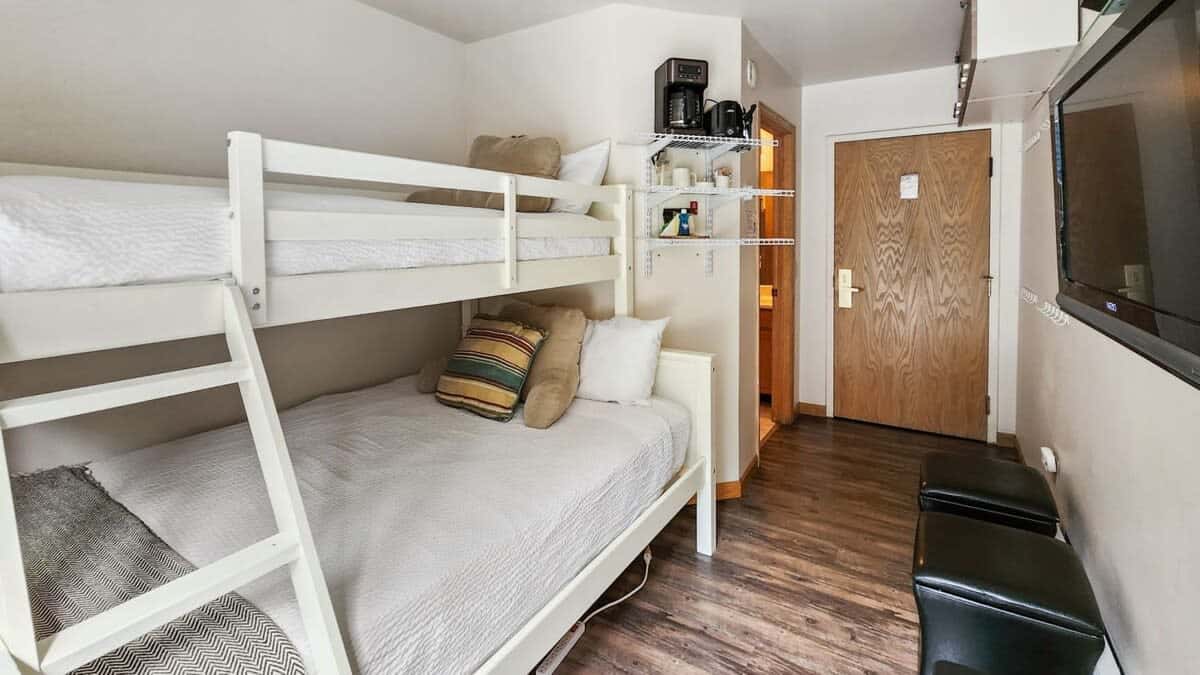 The studio features a bunk bed featuring a twin XL over a full-size mattress, a mounted TV, a full bathroom, and basic kitchen items for light meal prep.