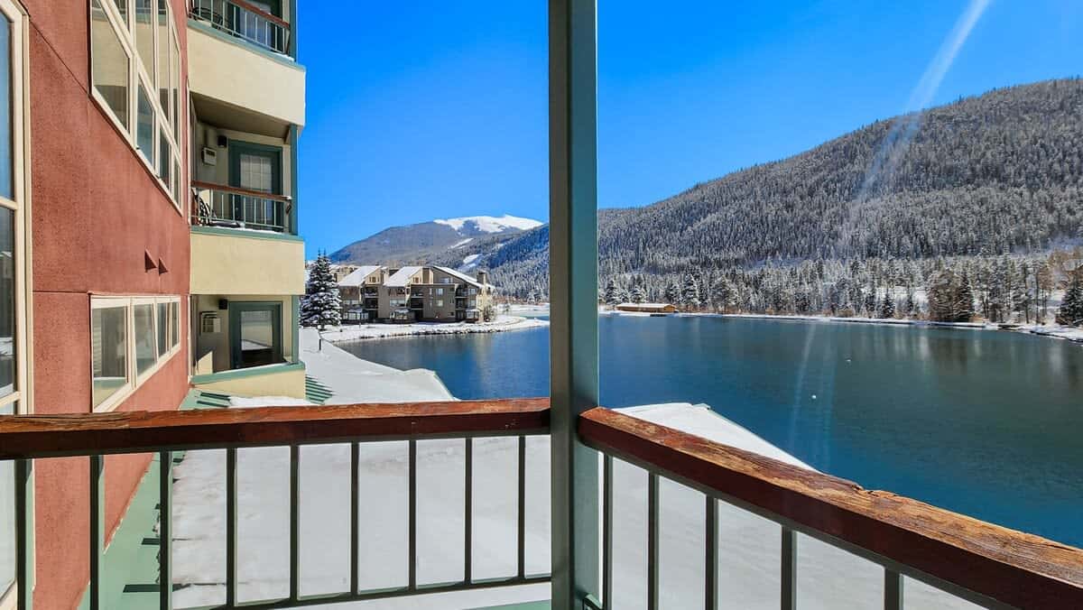 Large windows and a private balcony provide breathtaking views of the lake, mountains, and trees.