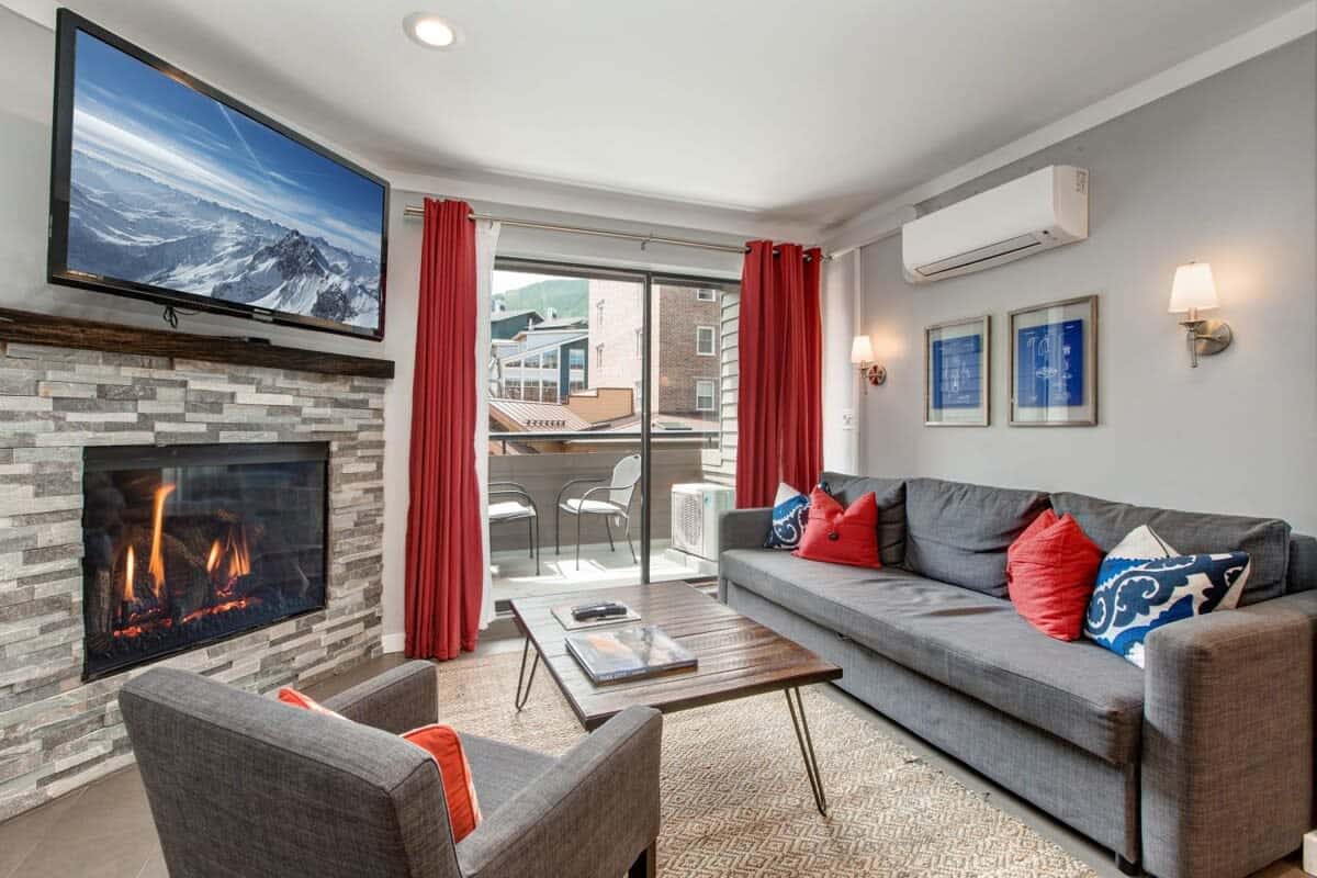 The fantastic living area with its large, flat-screen TV, plush couch that pulls out into a full-size bed, a cozy, modern armchair, roomy coffee table and outdoor patio with mountain village views.