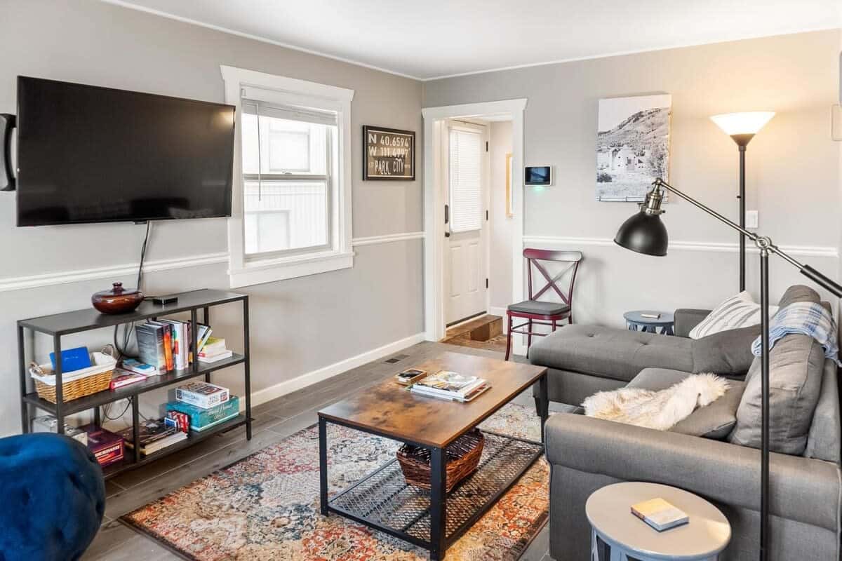 The intimate living room is a cozy space with a comfortable sectional sofa, an armchair and ottoman, a flat-screen TV, a gas fireplace, and a Murphy bed subtly tucked behind the wall of the sofa.