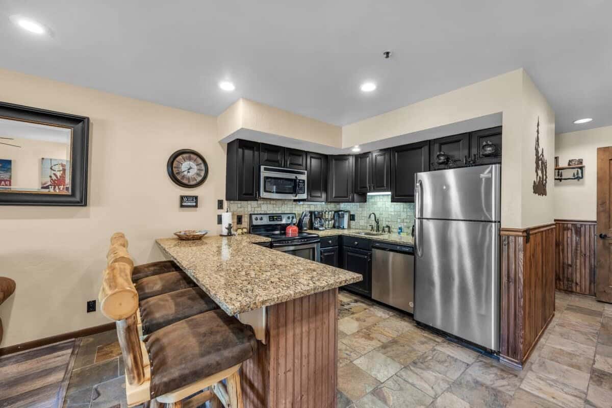 The condo features a fully equipped kitchen with stainless steel appliances, stylish all-black cabinets and granite countertops, and seating for four at the kitchen bar.