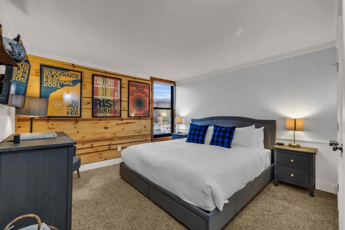 The inviting master bedroom is outfitted with a comfortable king-size bed, plush carpeting, matching nightstands, a dresser, and a mounted 43” smart TV.