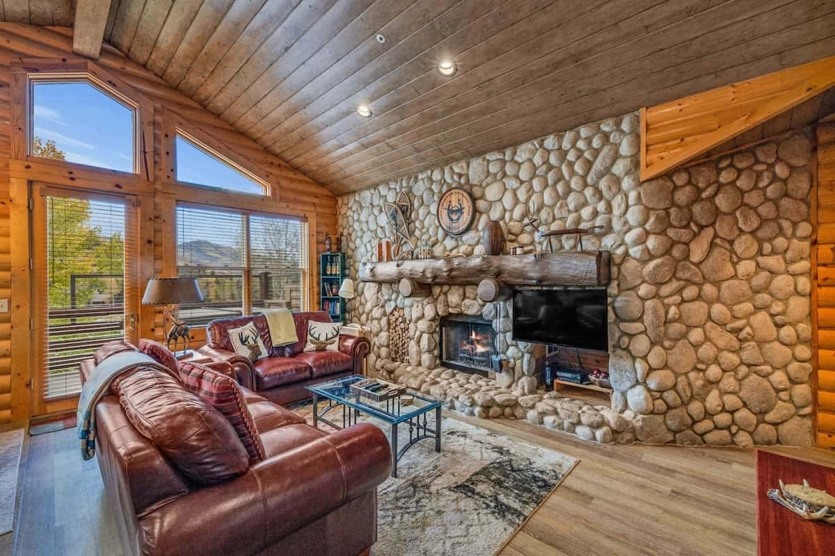 The home features an open floor plan with soaring windows providing a view of Deer Valley Mountain, an impressive stone hearth fireplace, and exposed wood beams.