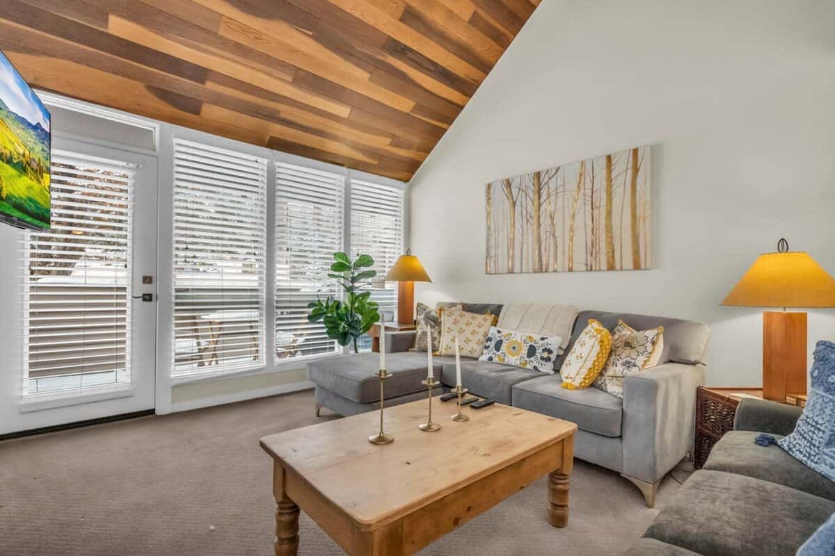 The living room boasts a warm ambiance with a vaulted, wood panel ceiling,a wood-burning fireplace, and plush furnishings.