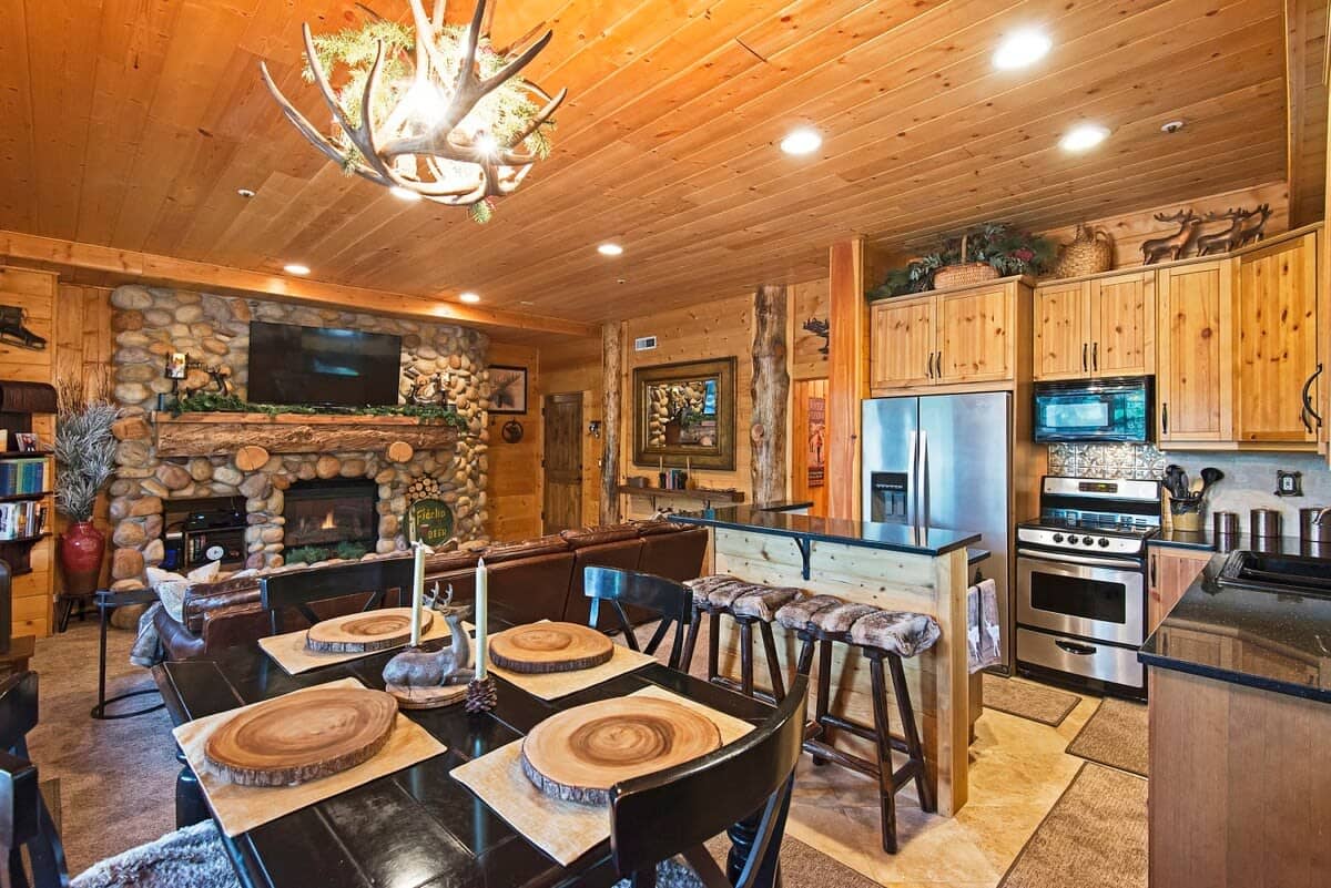 Classic cabin ambiance abounds in the open-concept kitchen/living/dining room area with its river rock fireplace and wood beam details. The kitchen boasts stainless steel appliances and a roomy island with bar seating.