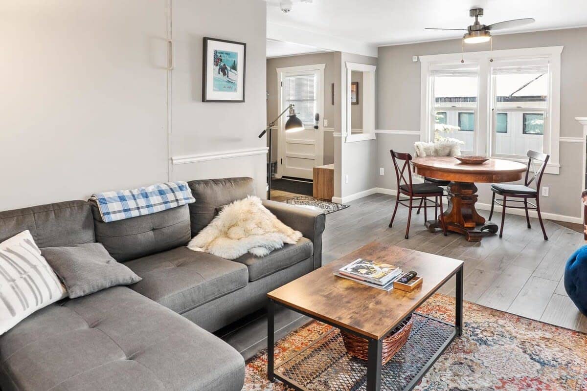 The combined living room and dining area boast a cozy sectional sofa, an armchair and ottoman, a flat-screen TV, a gas fireplace, a Murphy bed tucked behind the wall of the sofa, and a dining table with four chairs.