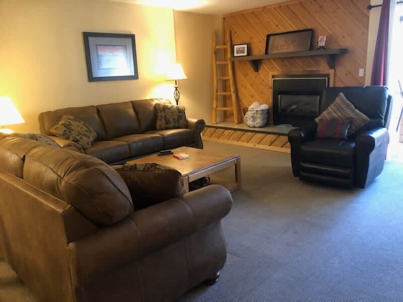 The cozy living area is full of classic cabin charm and ample plush seating between two couches, a coffee and a comfortable recliner, all surrounding the striking wood-paneled fireplace.