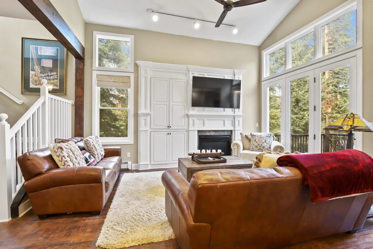 The stunning living room boasts high ceilings, picture windows, gorgeous built-ins surrounding the gas fireplace, a flat-screen TV,  coffee table, cozy armchair, end table, lamp and access to the outdoor deck with a gas BBQ grill.