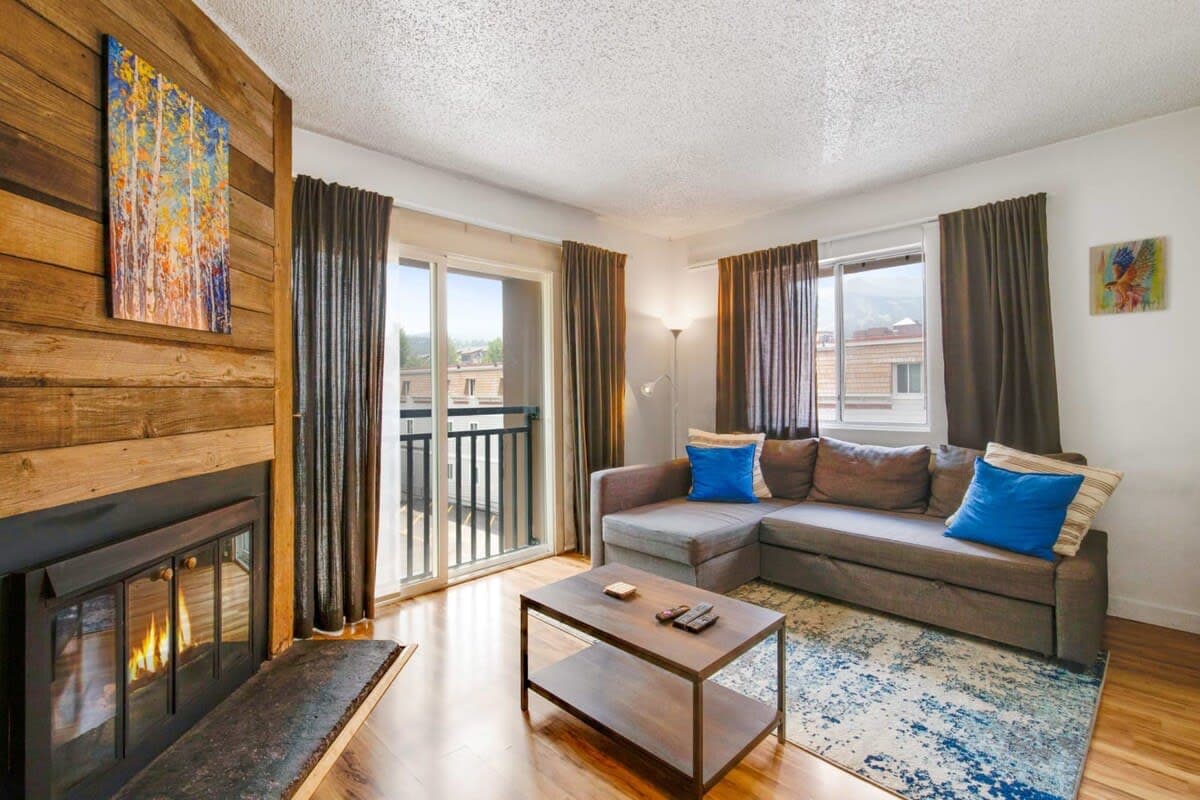 Relax in the living room with a comfortable couch, cozy wood fireplace, flat-screen TV, and access to the balcony