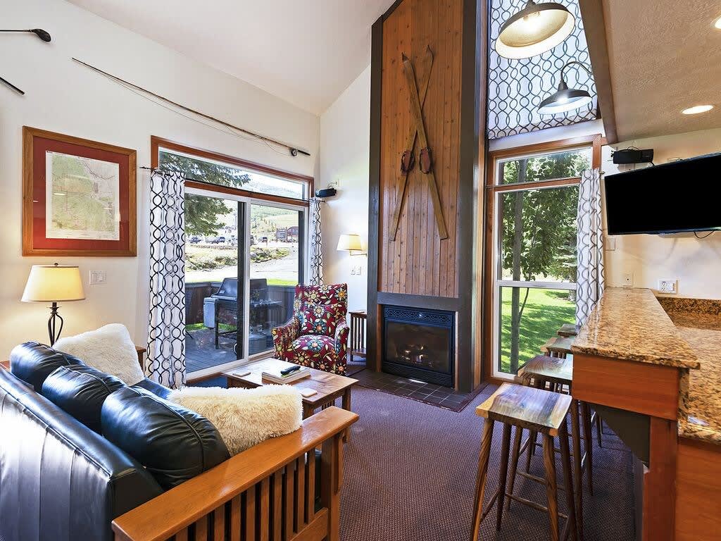 A leather couch, cozy armchair, striking wood-paneled fireplace, flat-screen TV and large windows highlighting this home’s terrific location with ski in/ski out access to Park City make for an inviting living space.