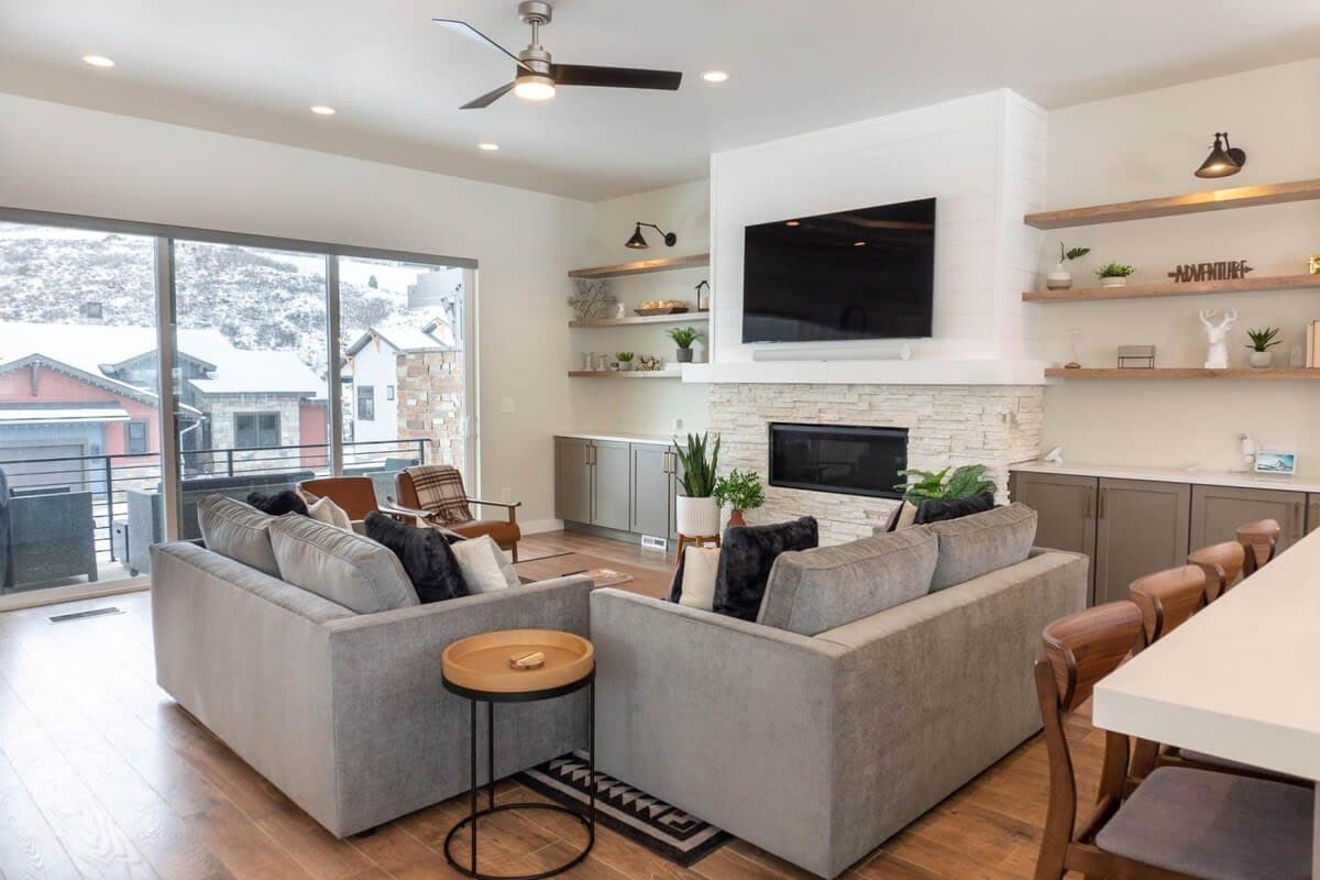 The living room is set up with everything you need for a relaxing space with an electrical fireplace, 65” smart TV, two sofas and two chairs, and well-placed decor creating a cozy home ambiance.