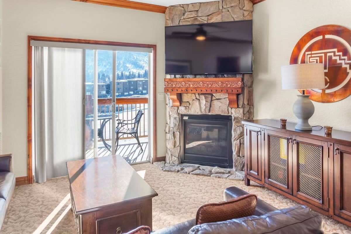 The charming living space offers a spacious common area for relaxing with two large couches, a 65” TV,  a lovely stone gas fireplace, and views out the balcony doors over Canyons Ski Resort.